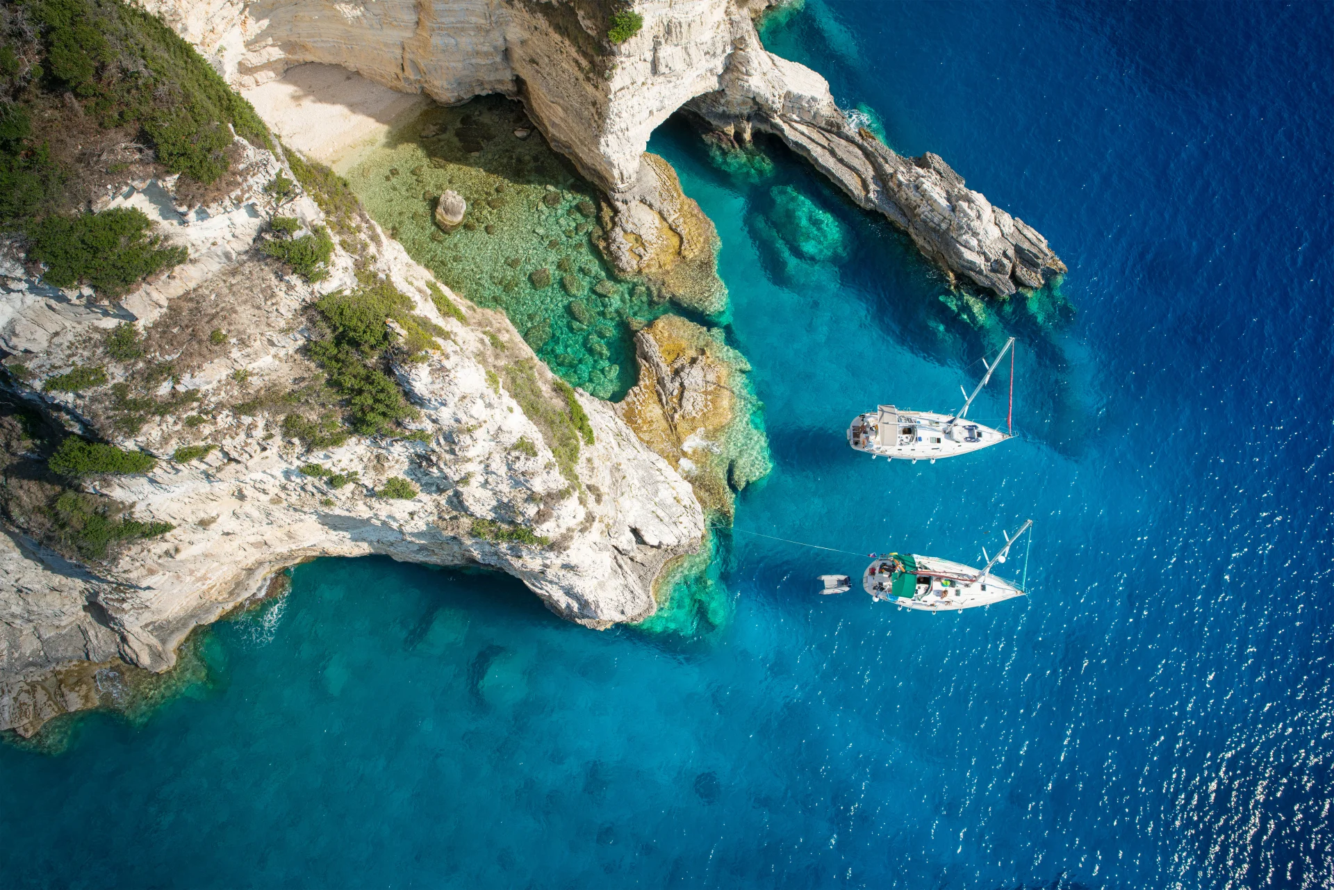 Sailboats anchored in a secluded turquoise cove with crystal-clear waters along the Greek coastline.
