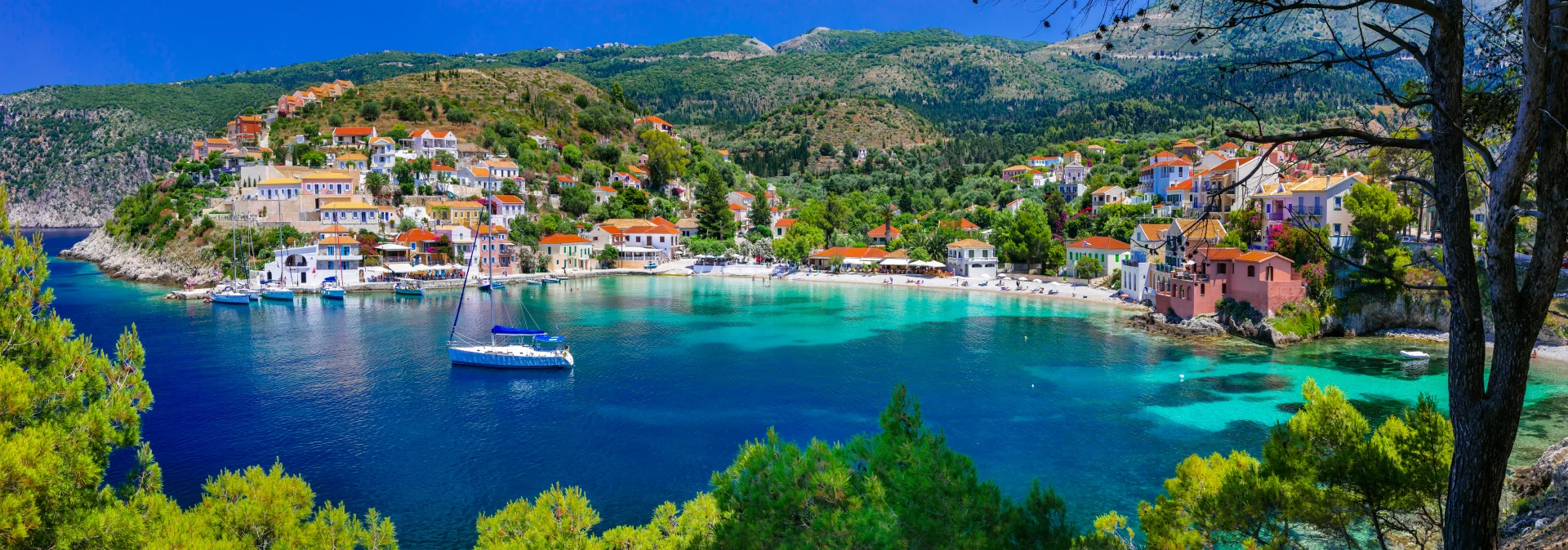 Charming Greek seaside village overlooking a peaceful bay with sailing yachts and crystal-clear water.