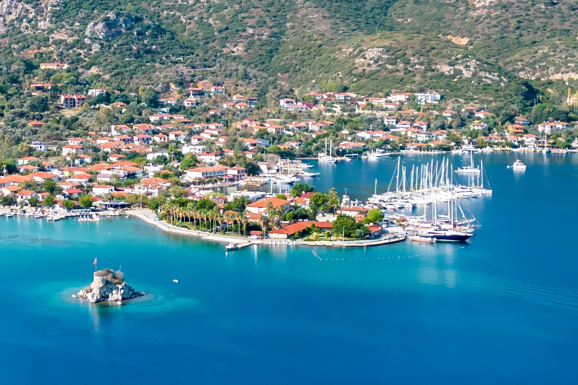 Scenic coastal view of Bozburun town, featuring red-roofed houses, a lively marina, and vibrant blue waters.