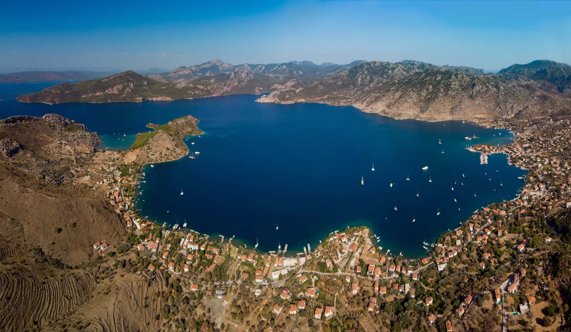 Panoramic aerial view of Bozburun's sheltered bay, surrounded by rugged mountains and dotted with yachts.