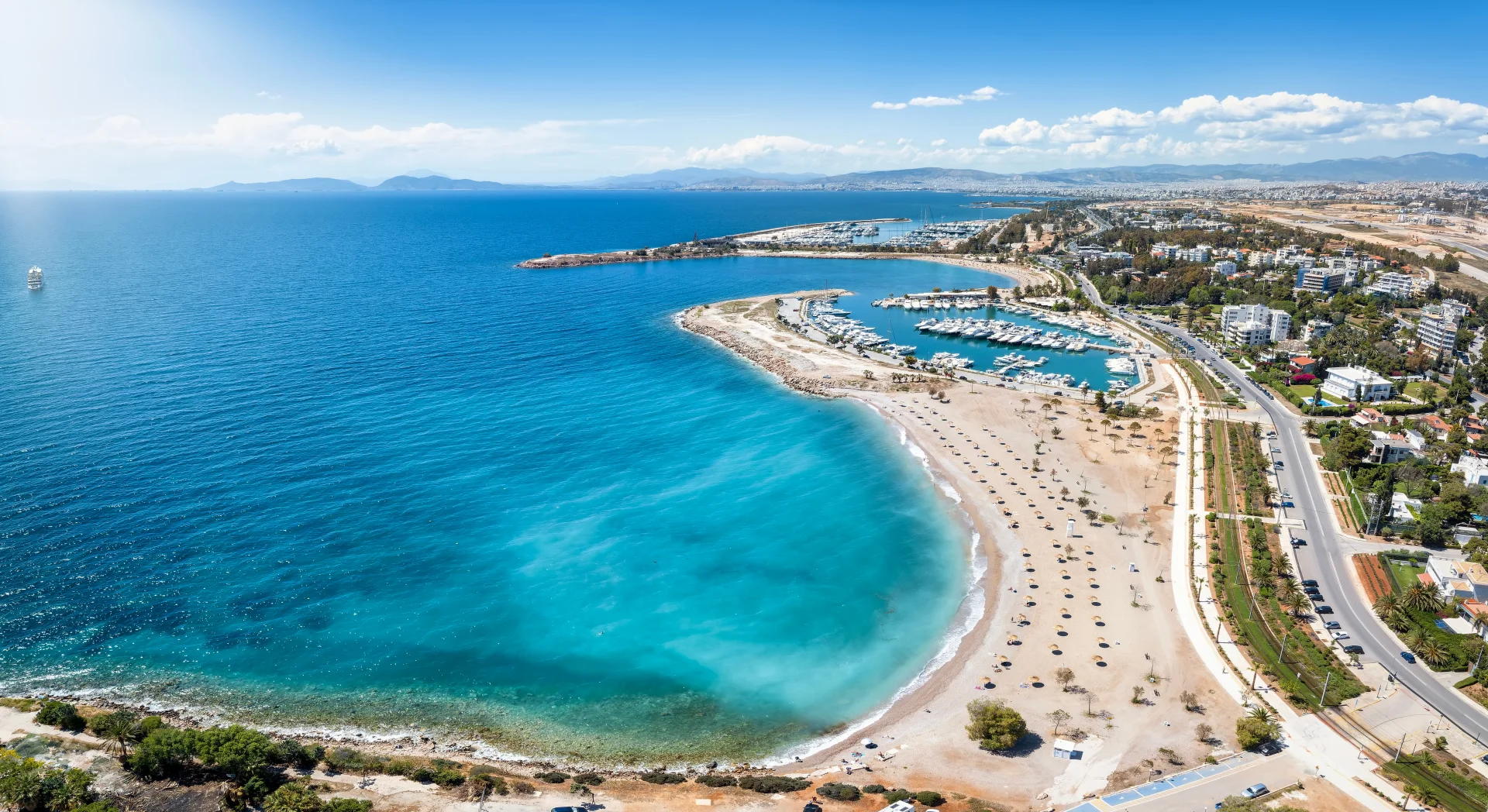 Panoramic aerial view of the Athenian Riviera, featuring a bustling coastal marina alongside sweeping sandy beaches.