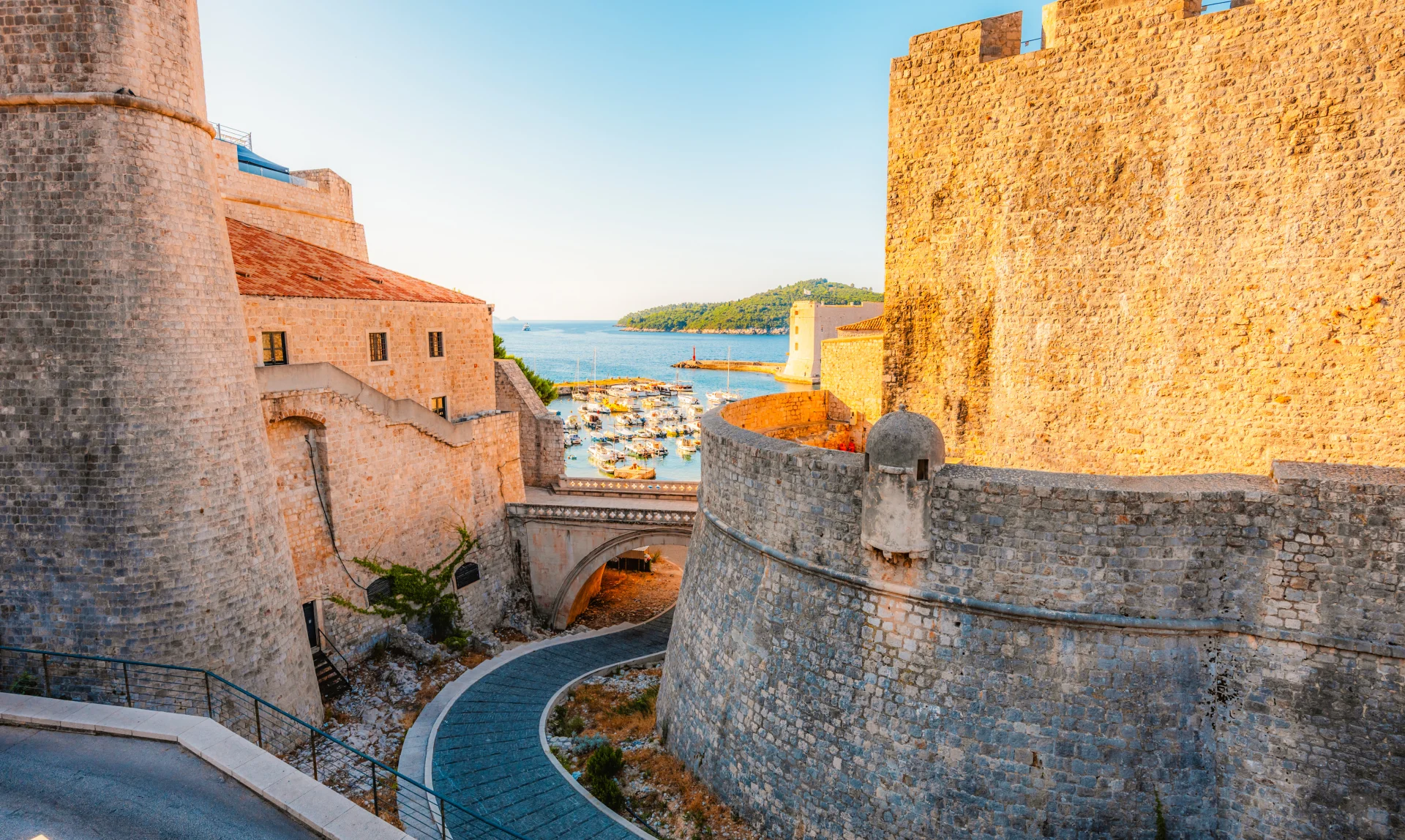 Golden hour sunlight illuminating the monumental stone city walls and historic harbor entrance of Dubrovnik.
