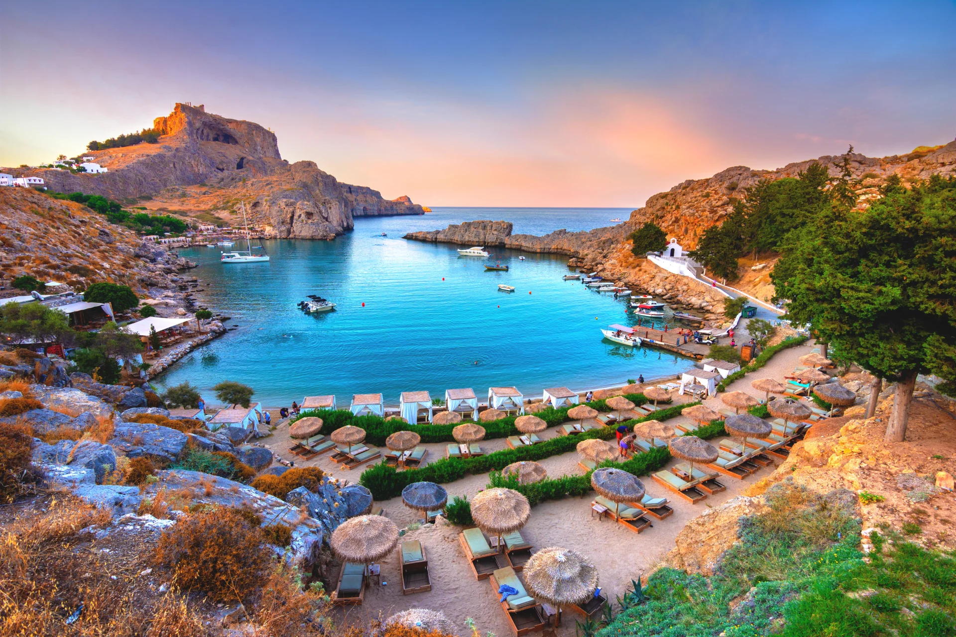 A stunning sunset illuminating the sheltered, rocky cove of St. Paul's Bay, a picturesque anchorage on the coast of Rhodes.