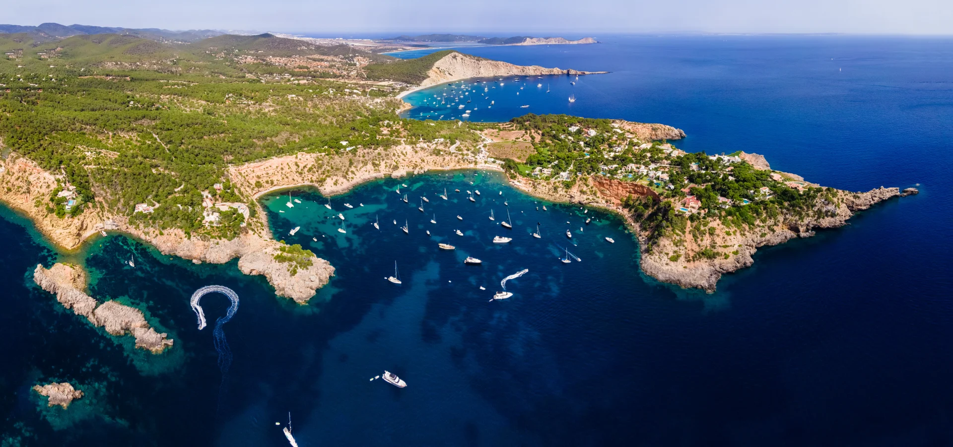 Aerial view of secluded anchorages and pine-clad peninsulas along the Turkish coastline, dotted with luxury yachts.